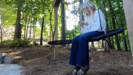 Adolescent Girl sitting on a swing out in nature, scrolling her phone