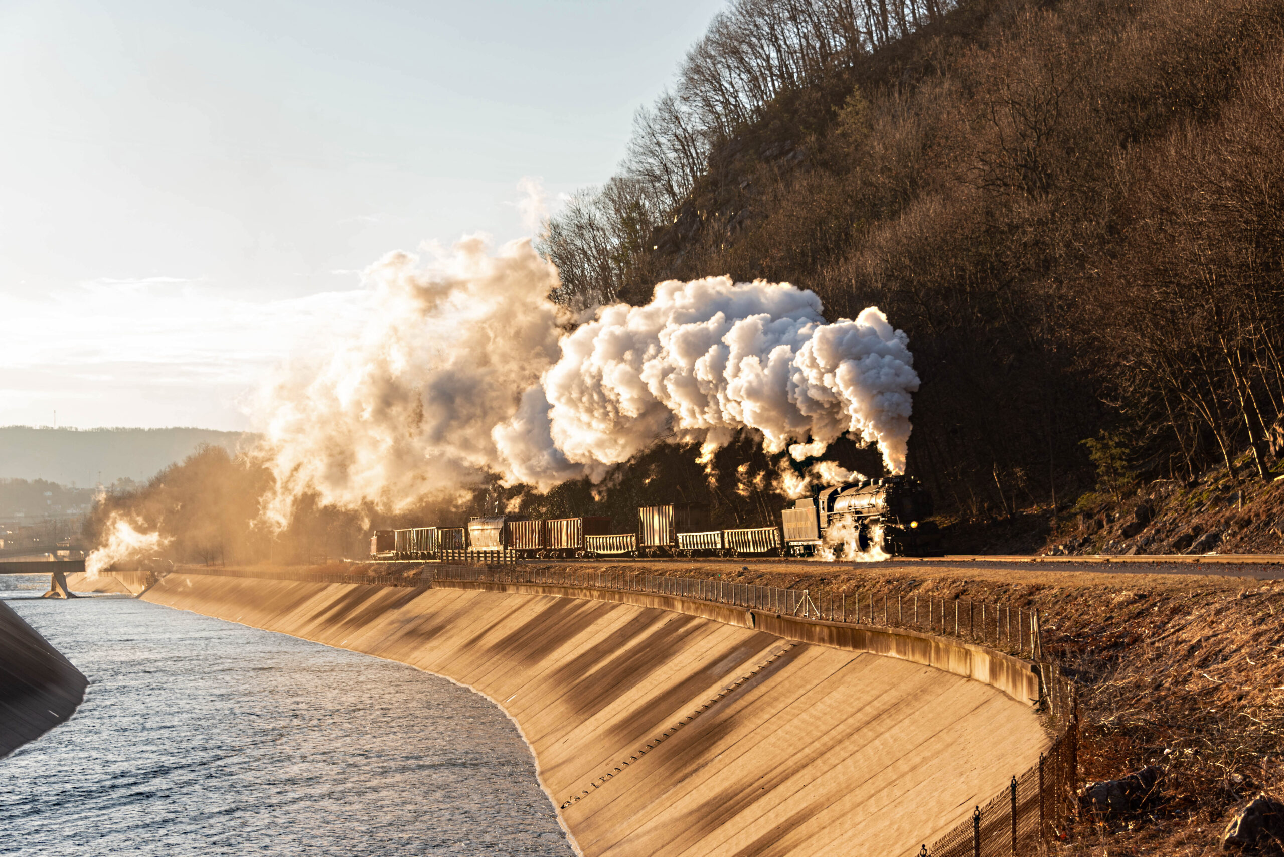 A train moving on a track with water to the left and a mountain to the right.