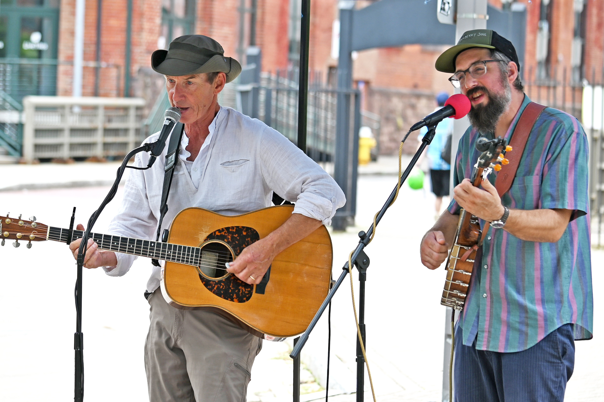 Two white men singing. The man on the left is strumming an acoustic guitar.
