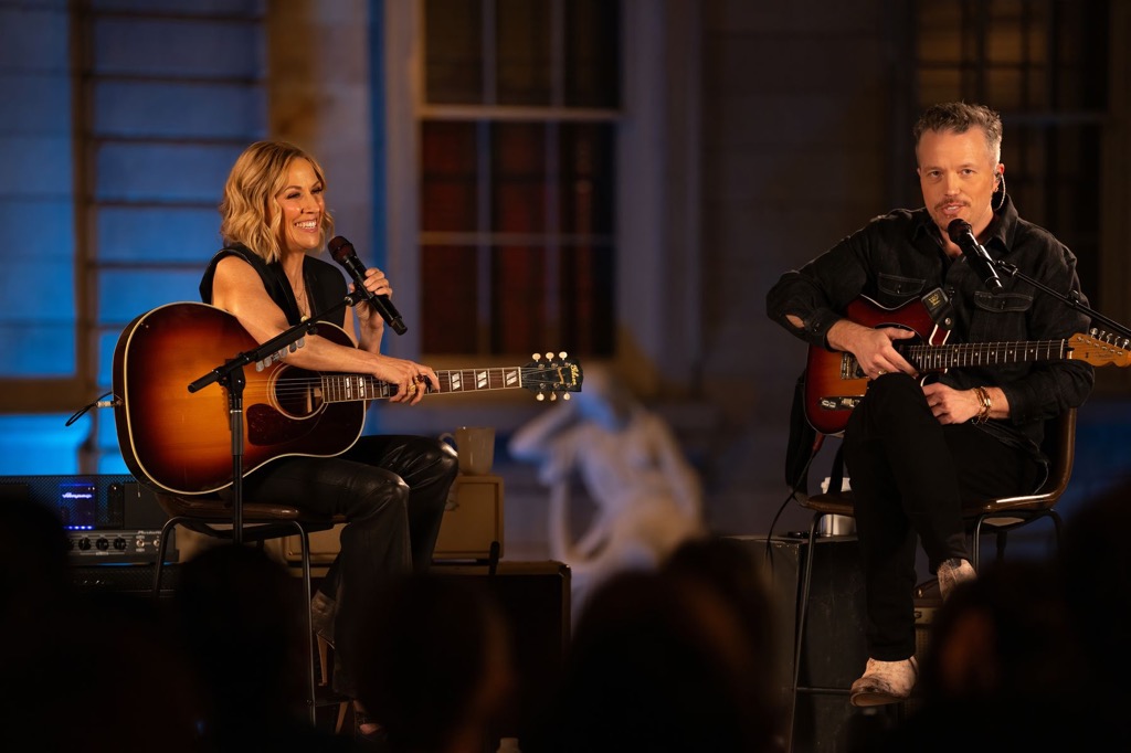 Musicians Sheryl Crow and Jason Isbell sitting on a stage with their guitars