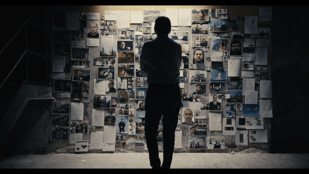 The back of man standing in front of a wall of photos and documents
