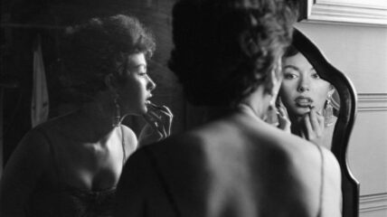 Picture of film and Broadway actor Rita Moreno as she puts on makeup in the mirror.