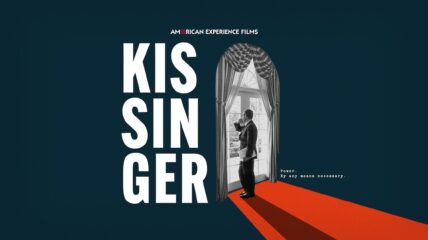 Kissinger looking out a window, standing on a red carpet