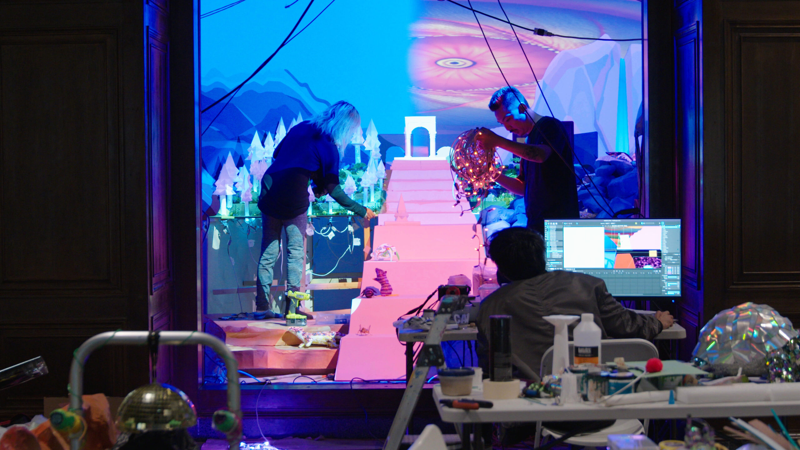 Two artists putting together a set that features a pink staircase.