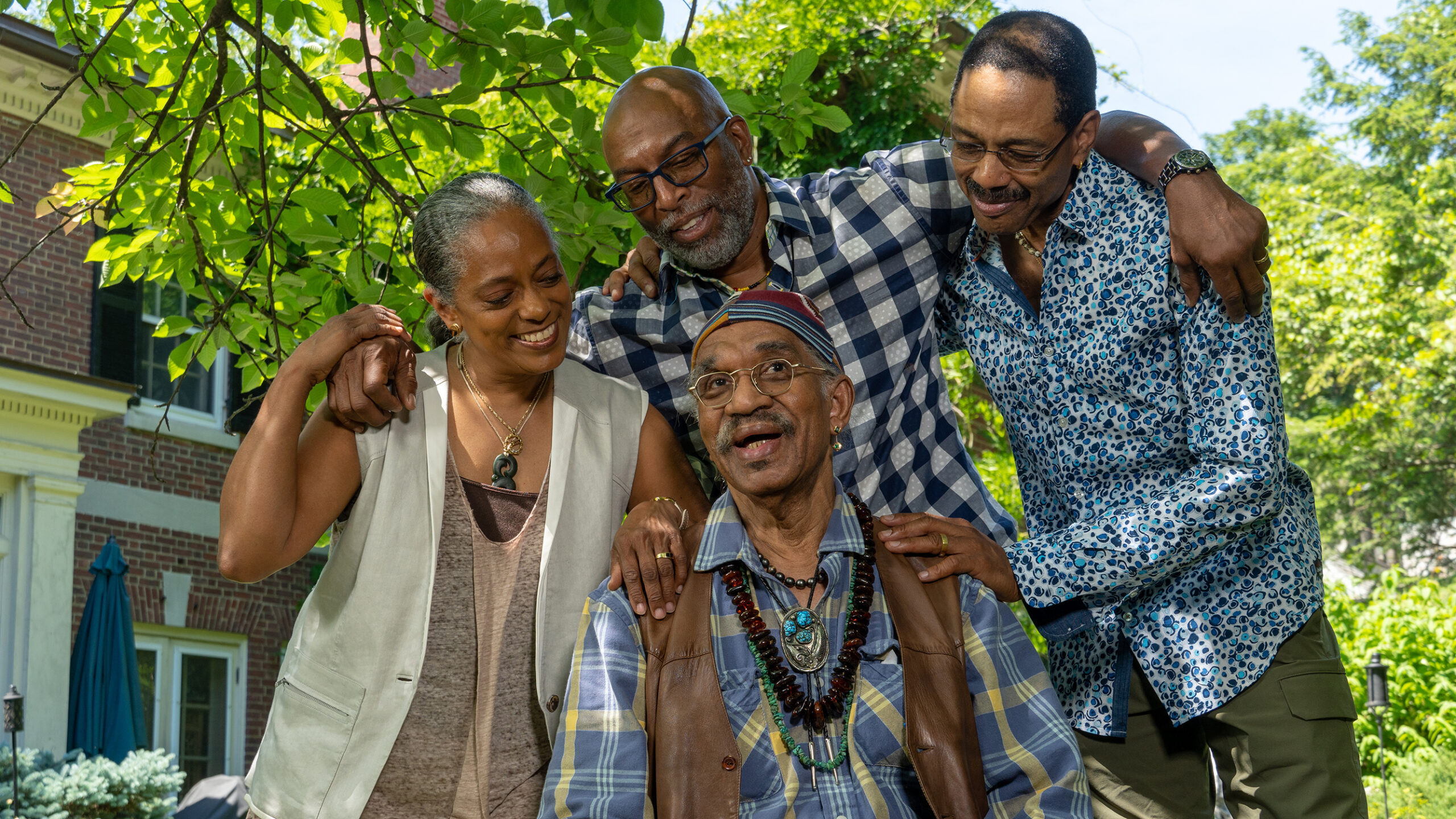 One Black woman stands with three Black men all smiling together.