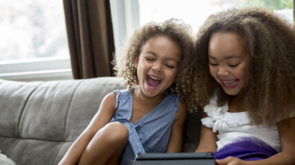 Two young girls sitting on a couch using a tablet.