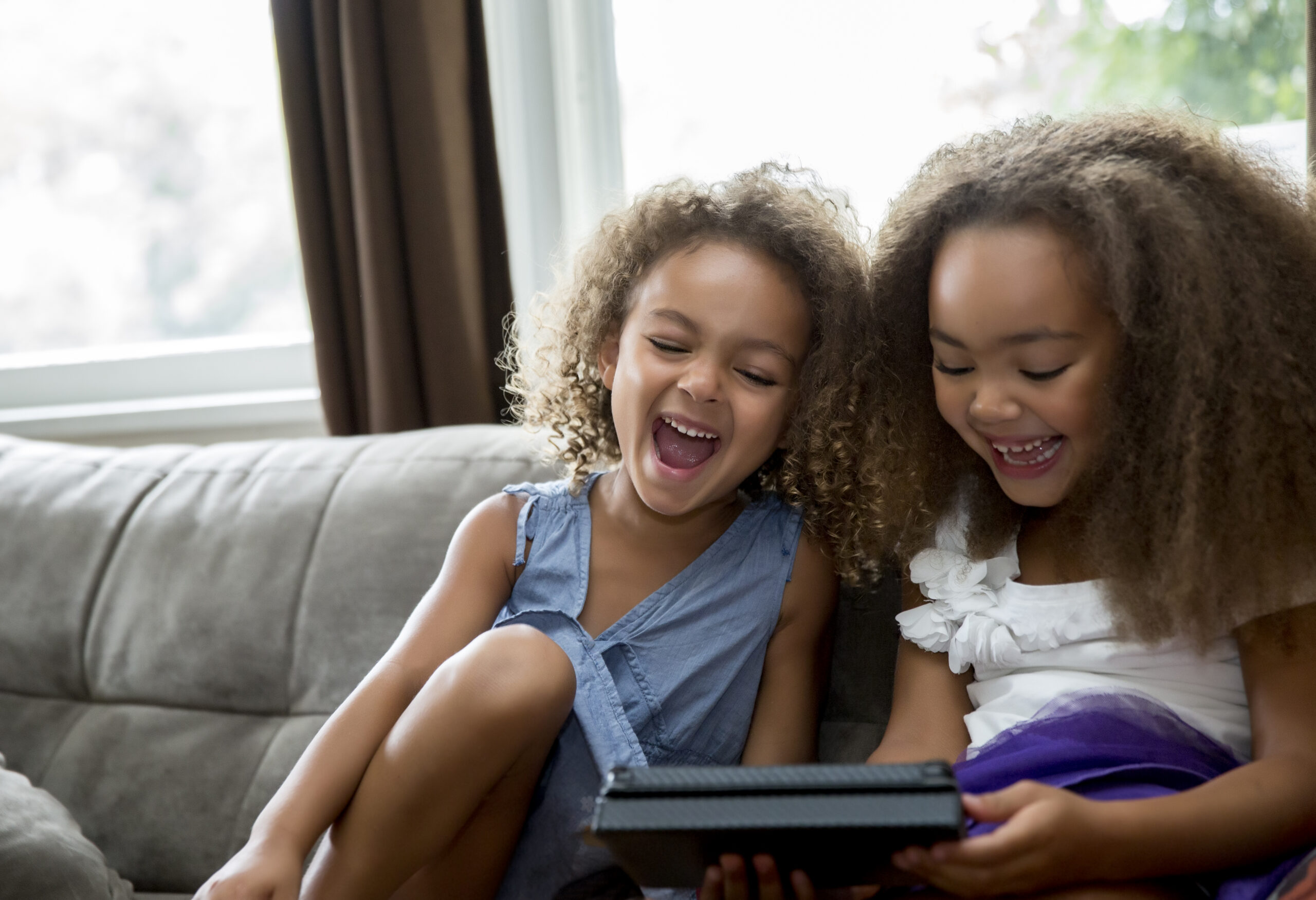 Two young girls sitting on a couch using a tablet.