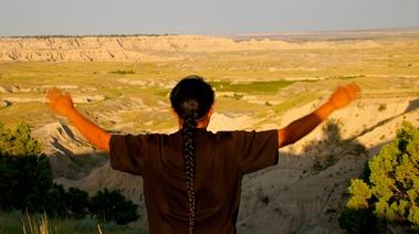 Urban Rez Man stands with his arm outstretched looking towards the horizon over a canyon