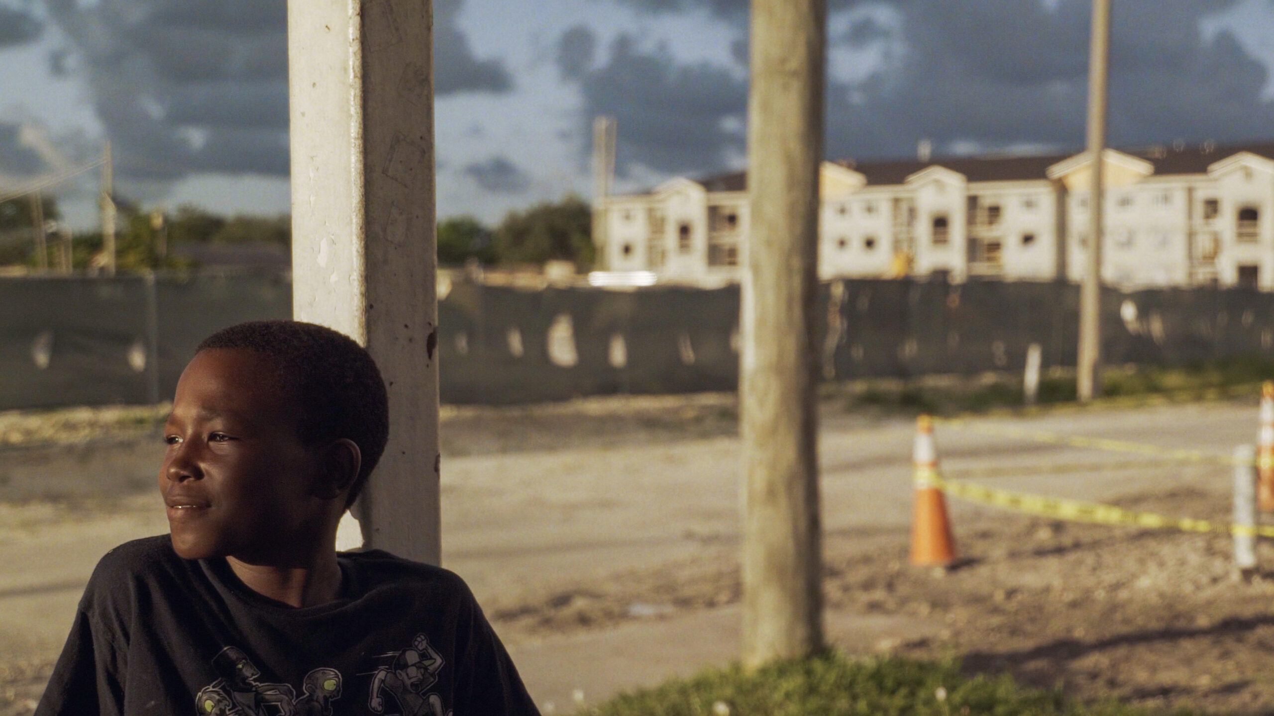Young Boy looks off into the distance. In the background is building complex and construction site