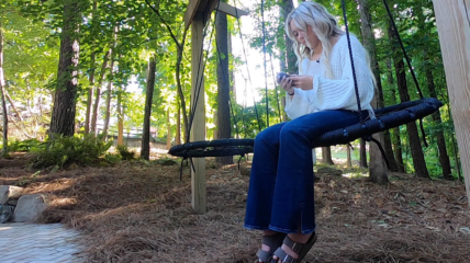 Adolescent Girl sitting on a swing out in nature, scrolling her phone