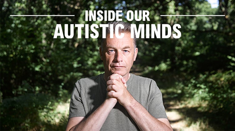 A shite male with salt and pepper short hair wearing a gray t-shirt looks at the camera with his hands clasped together under his chin.