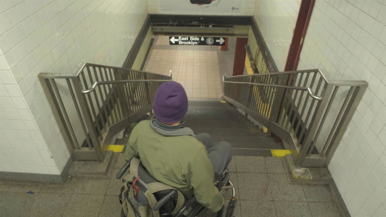 A photo of the back of a male in a wheel chair at the top of a flight of stairs.