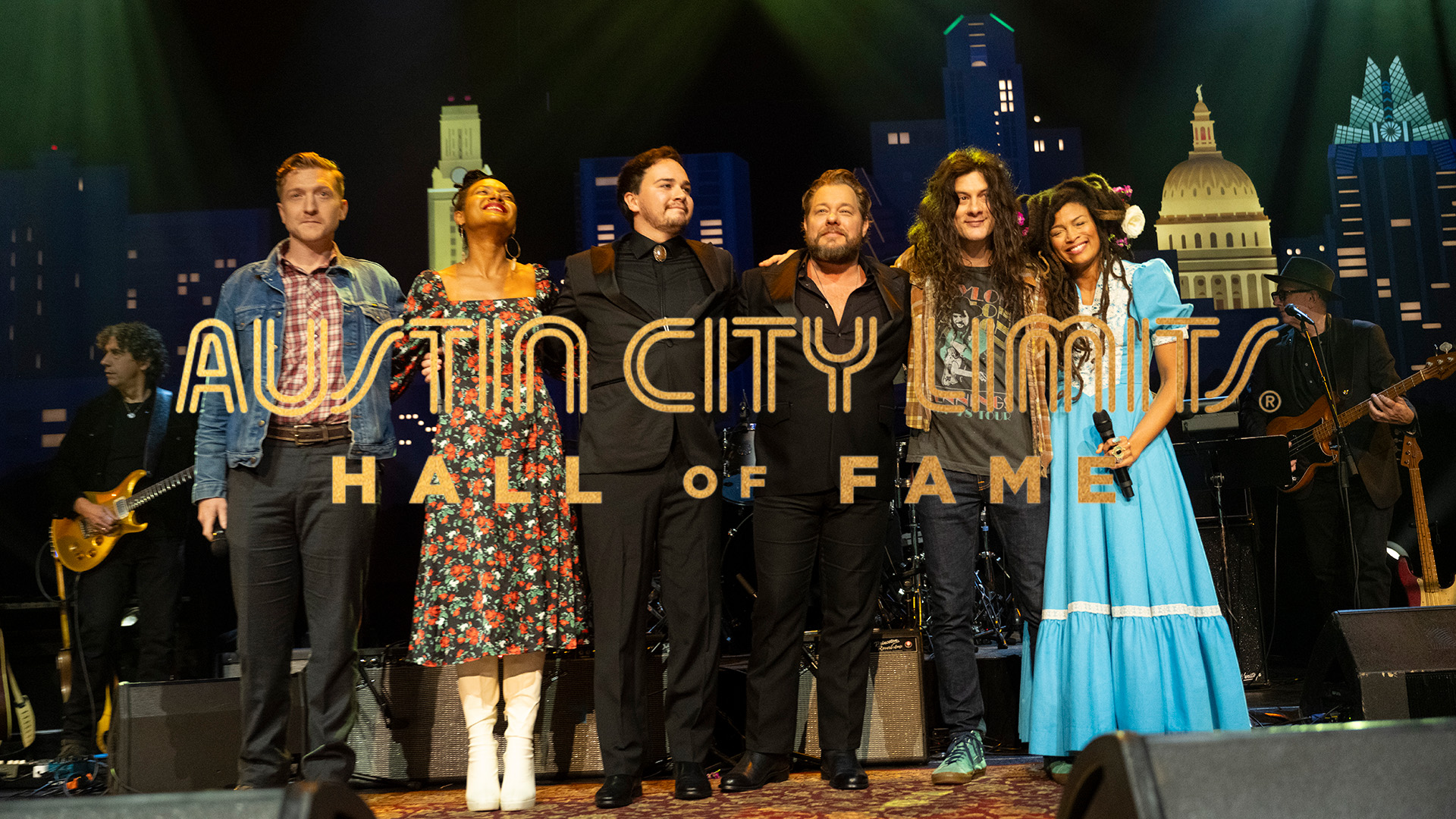 Six musicians stand on stage enjoying the applause