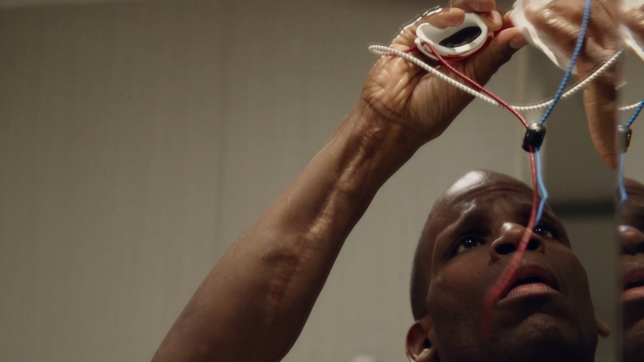 A Black man holding up and examining some wires.