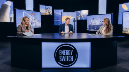 Two white woman and one white man sit behind a desk in a TV set.