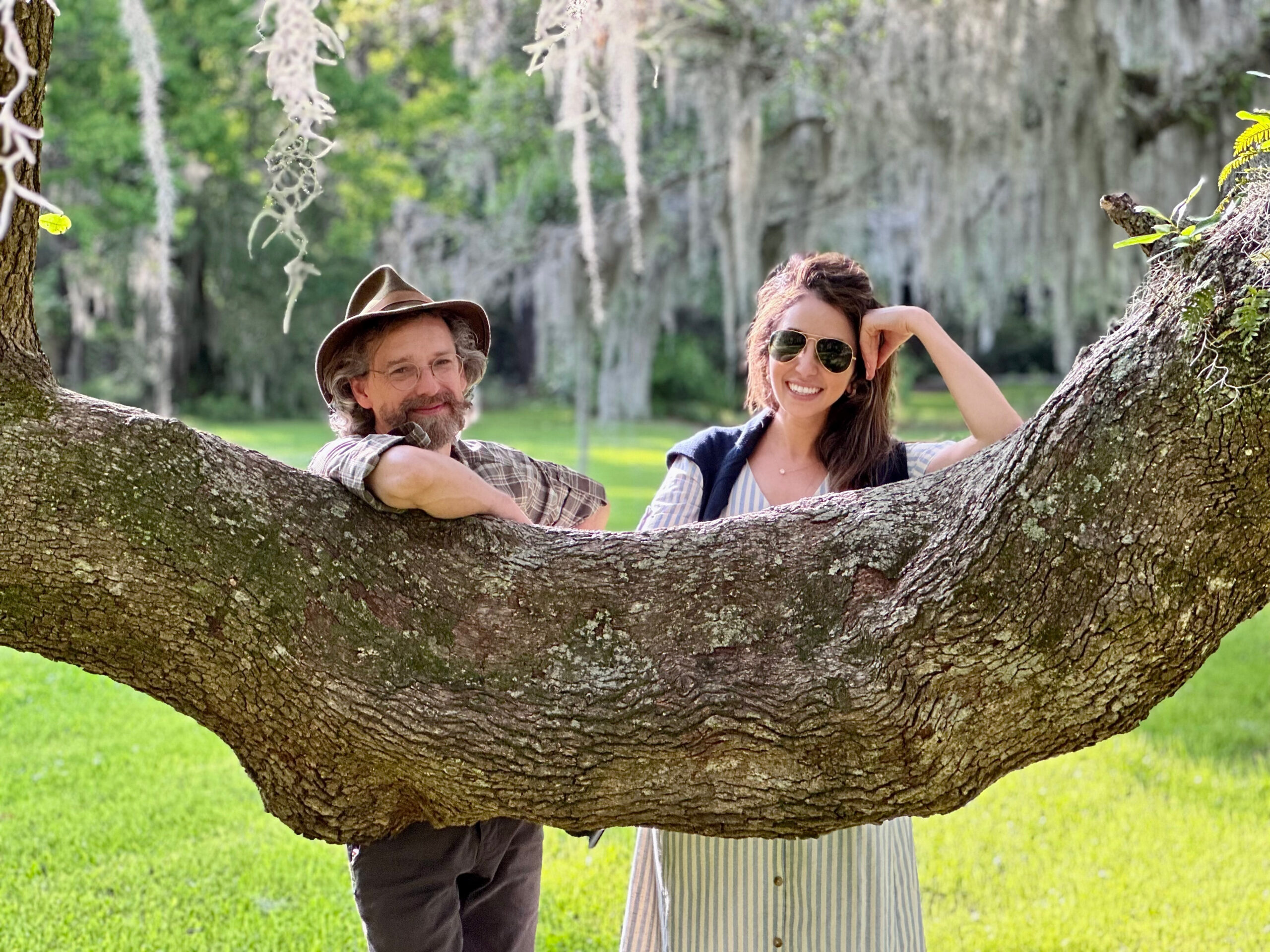 A white man in a brown flannel shirt and a brown hat has gray hair and beard. The white woman beside him has long brown hair and is wearing sun glasses.