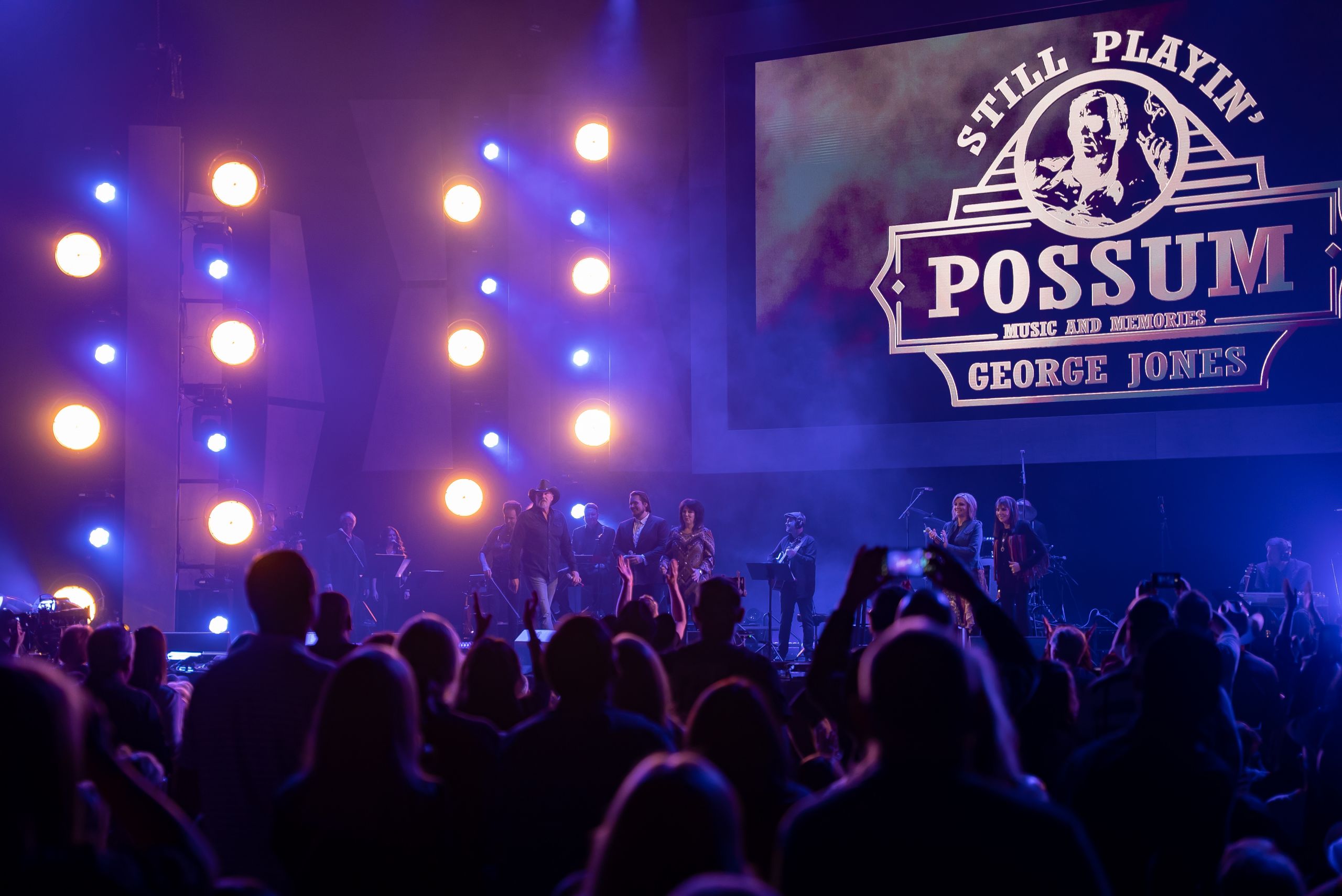 Stage shot with a band playing music. Sign above the stage reads: Still Playin' Possum Music and Memories George Jones.