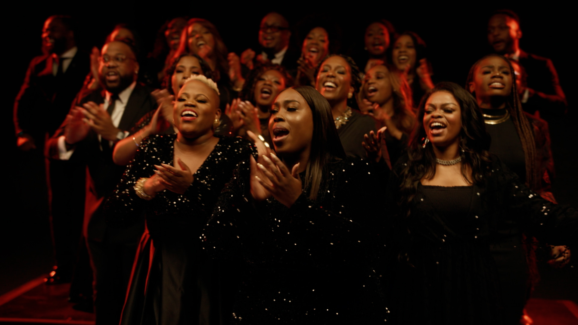 A choir of Black men and women wearing Black clothing, singing.