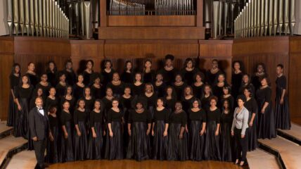 A group of Black female students that are part of the Spelman Glee club, all wearing Black dresser stand in four tiered rows.