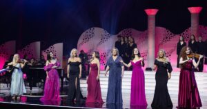 8 female musicians in long gowns stand on stage performing