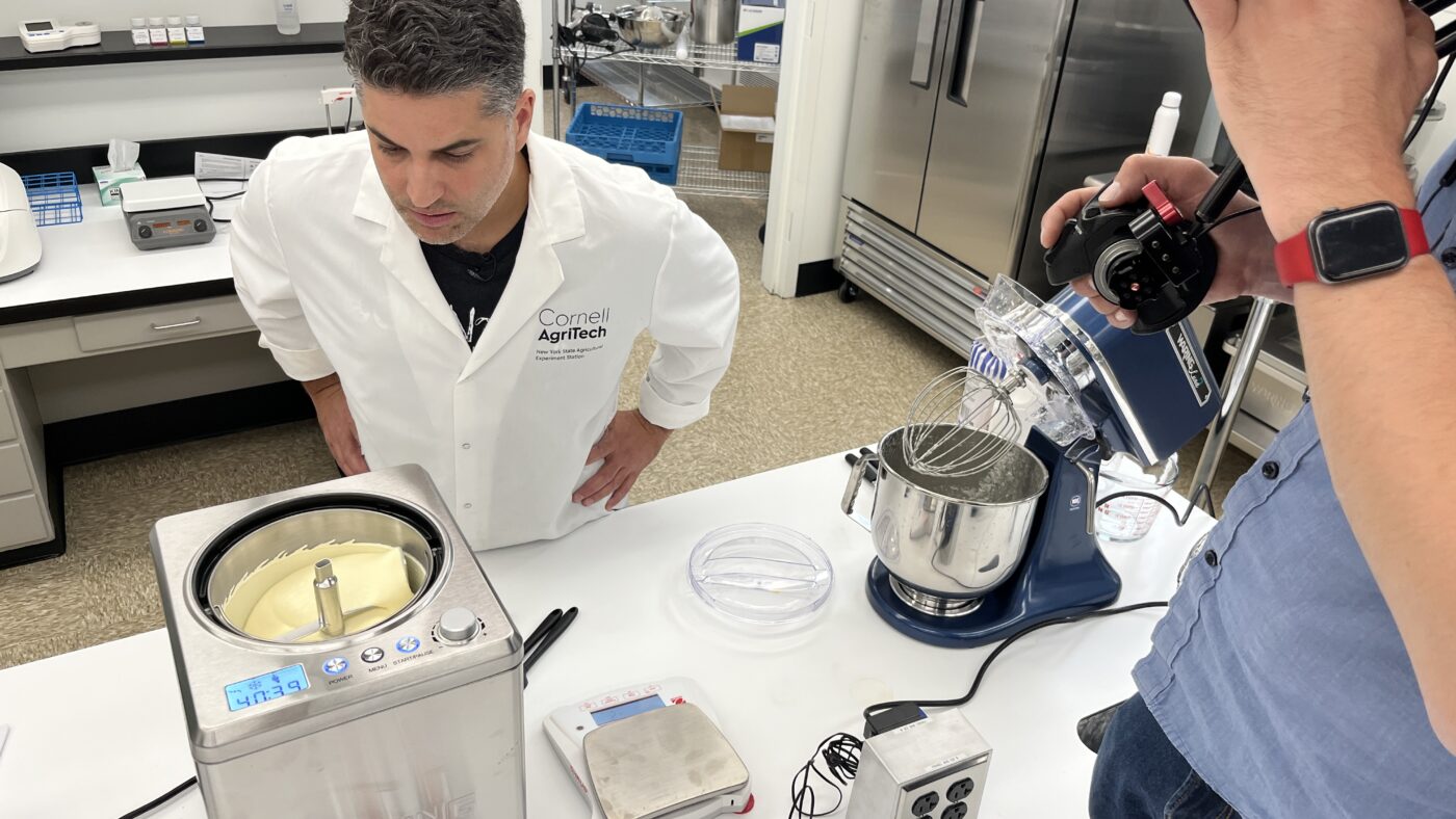 Man in a lab coat checking the ice cream maker and being filmed