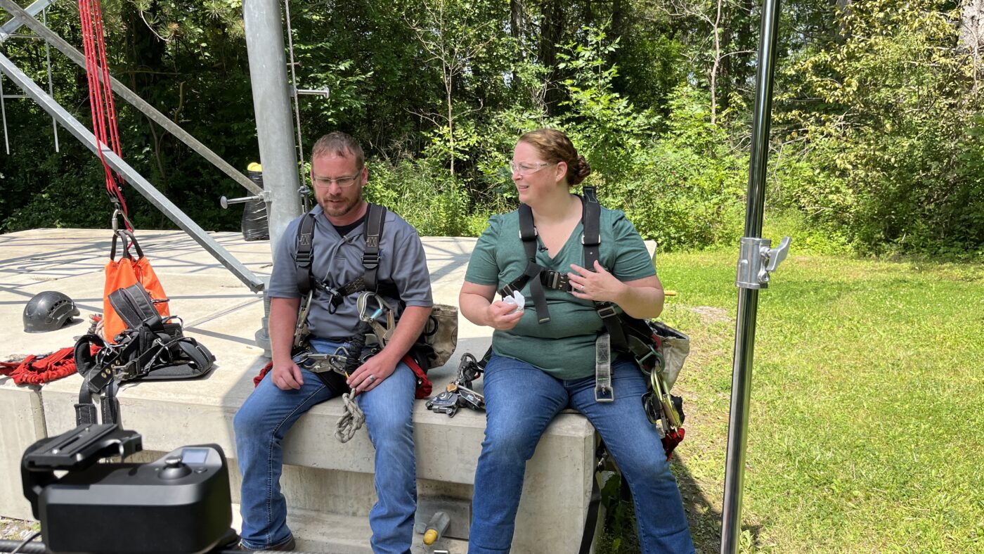 Man and woman putting on safety harnesses for a tower climb