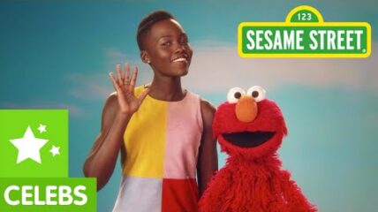 Sesame Street Celebs A black woman waves with Elmo, a red puppet next to her