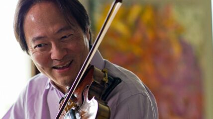 An Asian man with dark hair wearing a purple collared shirt playing the violin