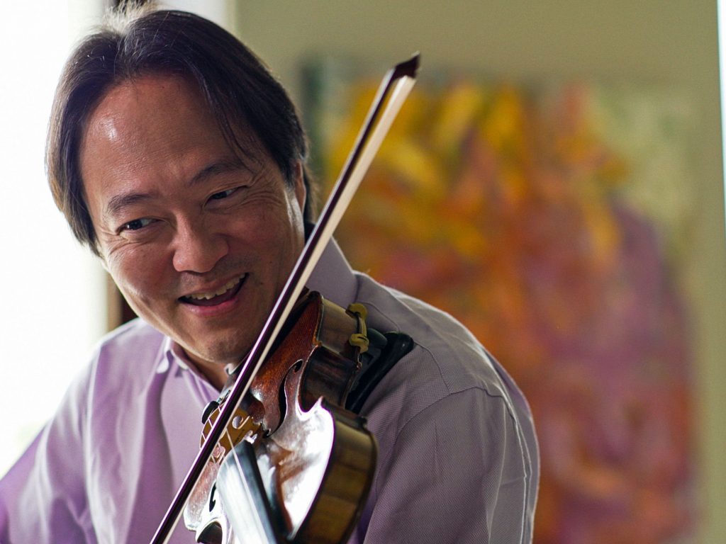 An Asian man with dark hair wearing a purple collared shirt playing the violin