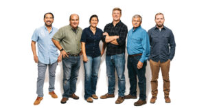Six people standing together - five men and one woman all wearing jeans and button down collared shirts