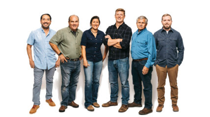 Six people standing together - five men and one woman all wearing jeans and button down collared shirts