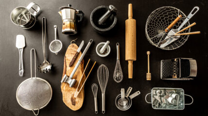 A bunch of kitchen tools placed on a Black counter - including a wish, rolling pin, measuring cups collander