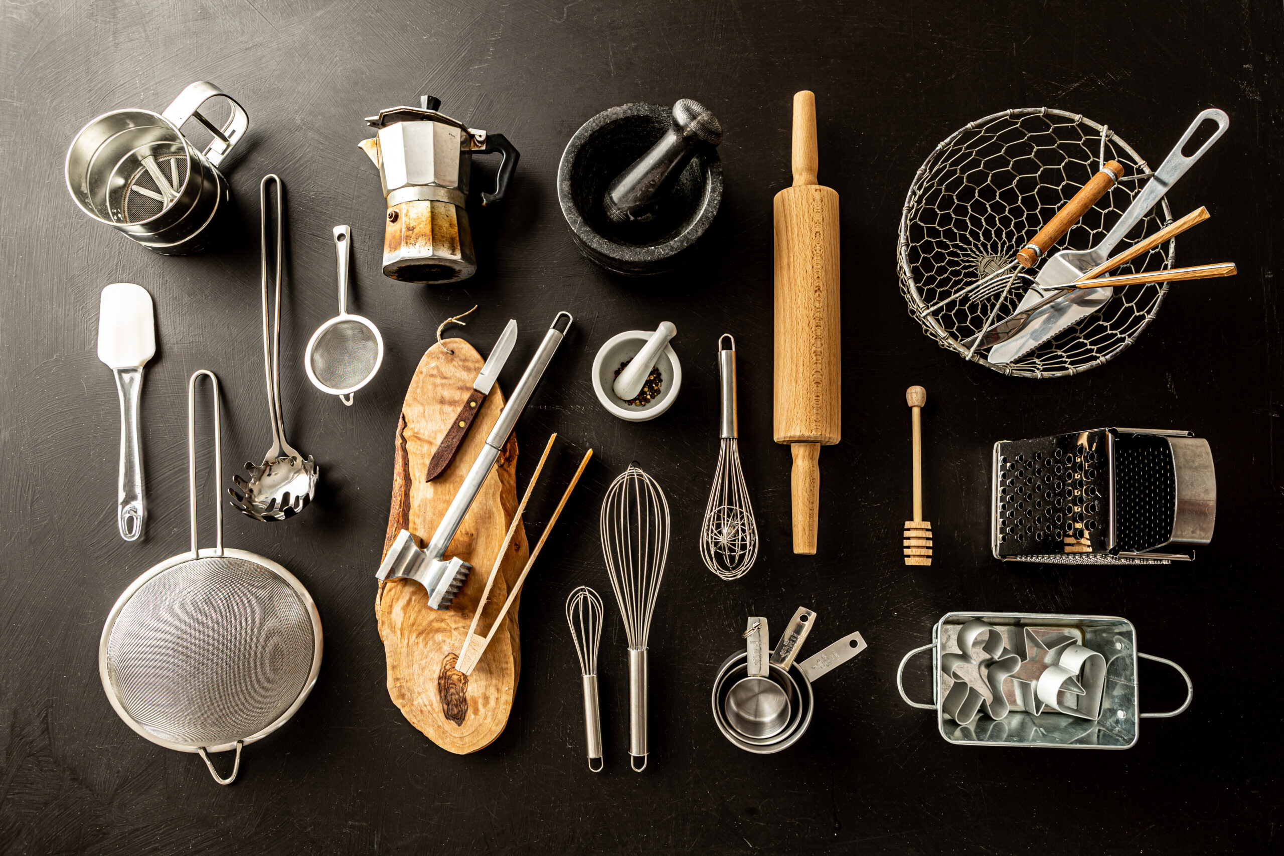 A bunch of kitchen tools placed on a Black counter - including a wish, rolling pin, measuring cups collander