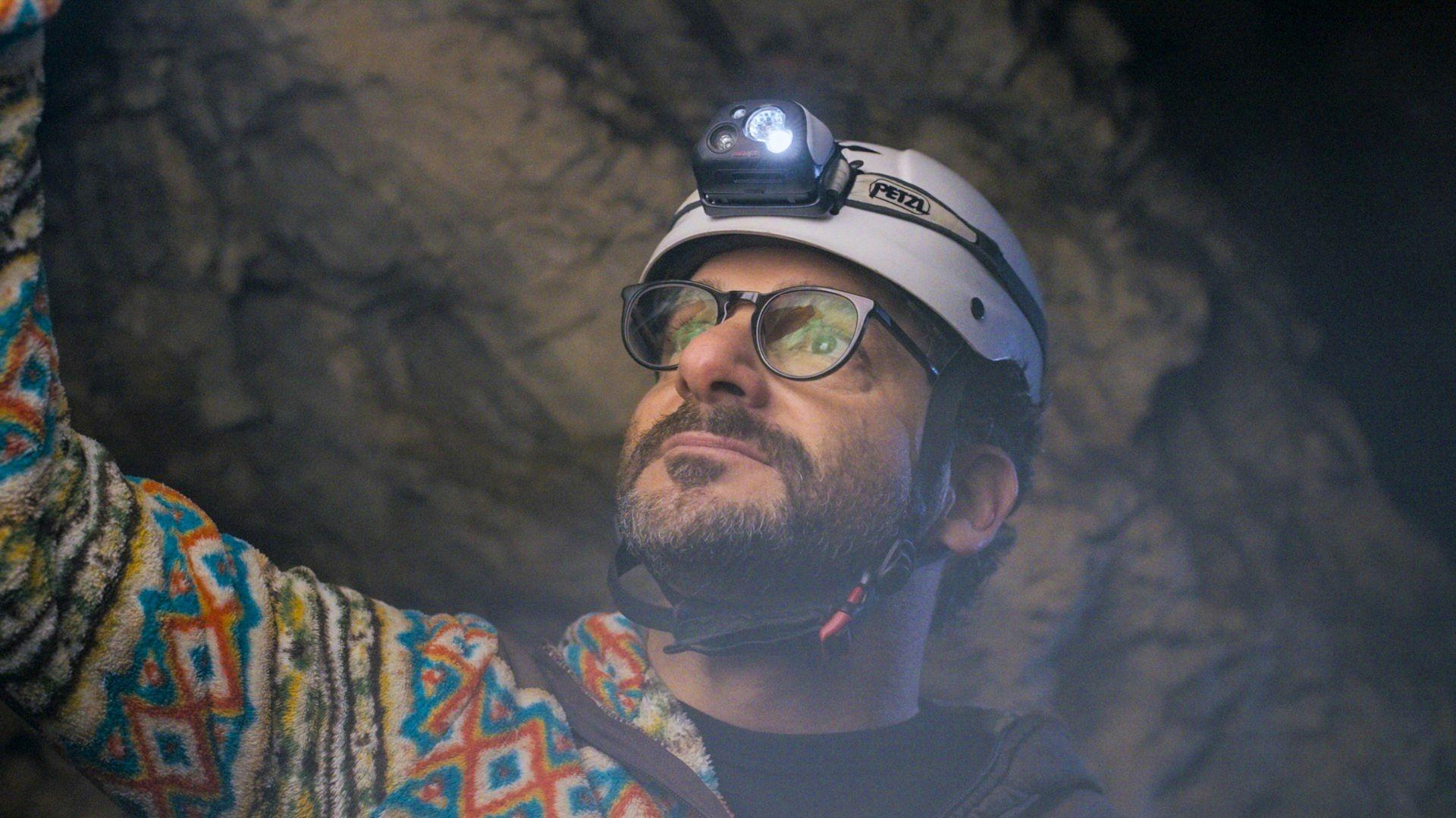 A white male wit a brown mustache and beard wearing a hard hat and headlight.