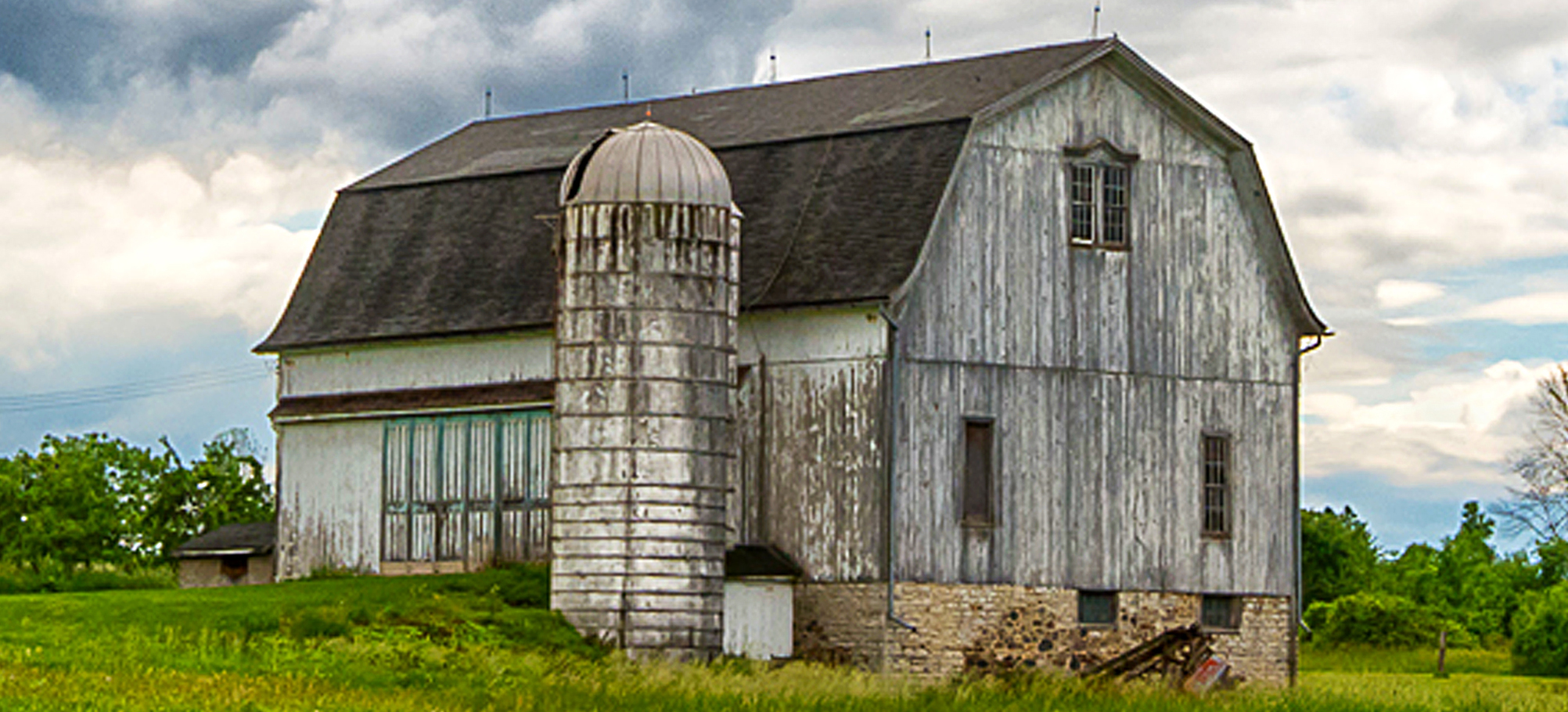 A white barn with a dark brown roof and a shite silo on a farm
