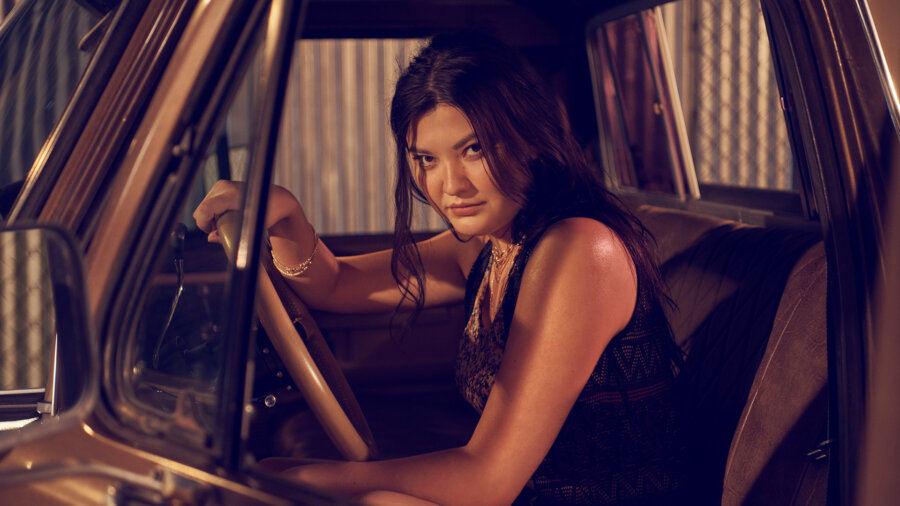 A young Russian women with long brown hair sits behind the steering wheel of a car.