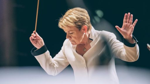 Conductor Marin Alsop wearing a shite blouse with Black cuffs conducts.