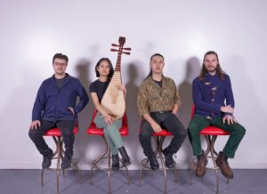 Four band members sit on a row of red chairs