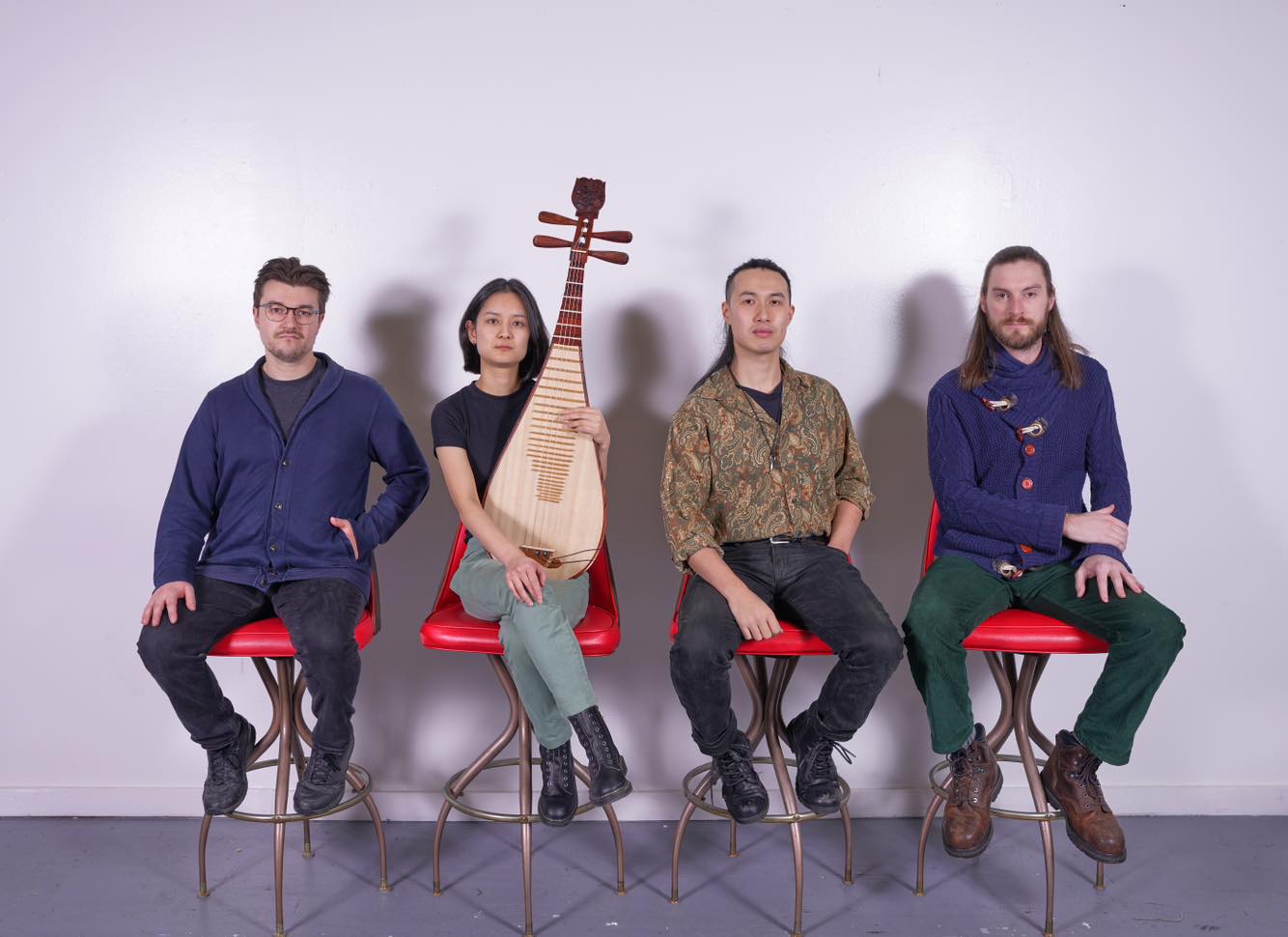 Four band members sit on a row of red chairs