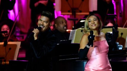 Singer Sheléa in a pink longs strapless dress singing on stage.