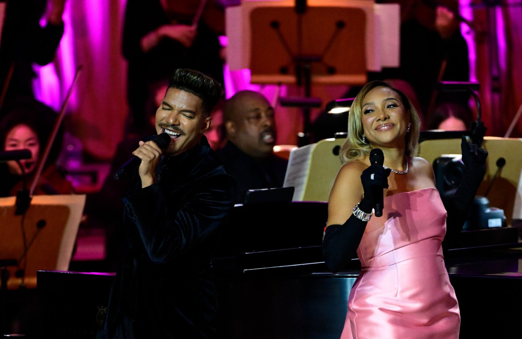 Singer Sheléa in a pink longs strapless dress singing on stage.