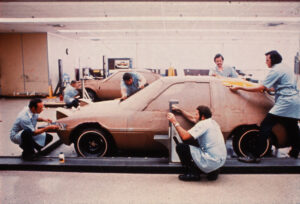A bunch of mechanics working on the body of a Pacer car.