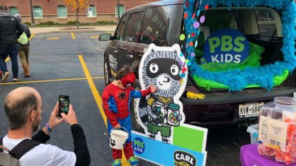 Adult taking picture of child dressed in costume at Halloween trunk or treat event.