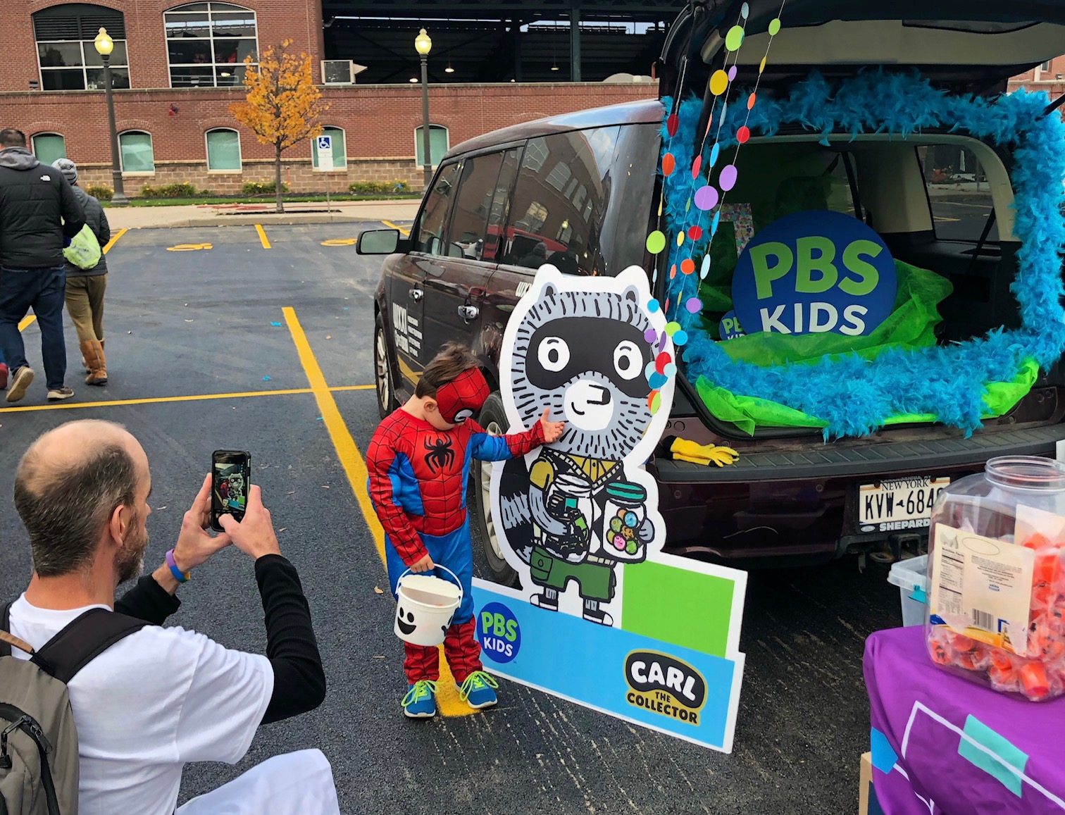 Adult taking picture of child dressed in costume at Halloween trunk or treat event.