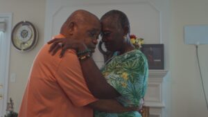 An older Black man and woman slow dancing as their heads lean against each other.