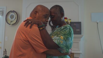 An older Black man and woman slow dancing as their heads lean against each other.