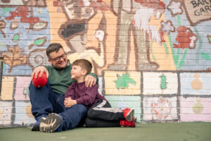 A Dad and his young son sit together in front of a mural.