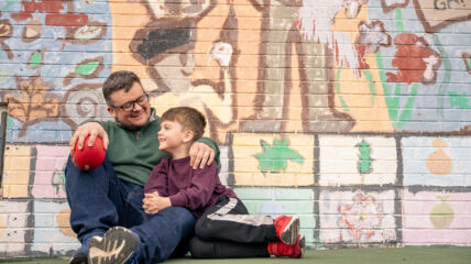 A Dad and his young son sit together in front of a mural.