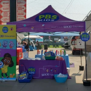 Image shows the WXXI Education purple tent and table display at a Rochester community event.