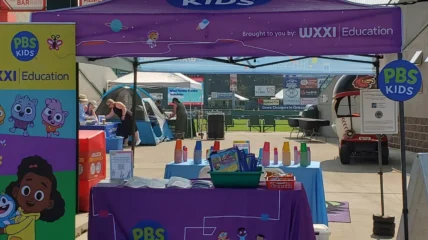 Image shows the WXXI Education purple tent and table display at a Rochester community event.